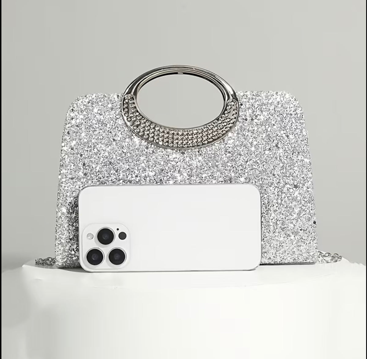 Silver evening bag shown next to a phone